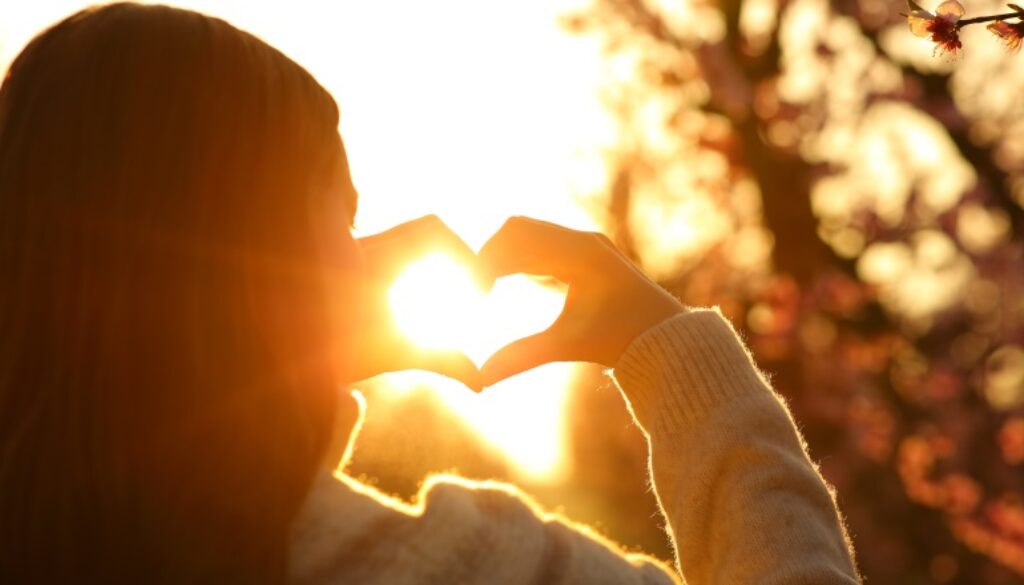 Woman hands making heart shape at sunset