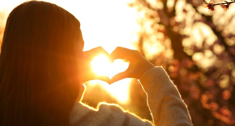 Woman hands making heart shape at sunset